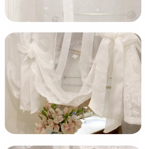 Dettaglio tenda in pizzo bianco con ricamo floreale e fiocchi decorativi nastro