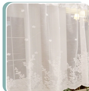 Close-up of white lace curtain showing floral embroidery and scalloped edges