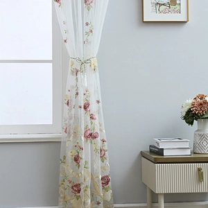 White sheer curtain with red floral rose embroidery and green leaf patterns in sunlight