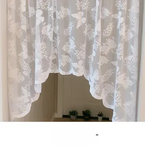 Close-up of white lace curtain featuring rose and butterfly embroidery with scalloped edges