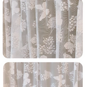 Detail of white lace curtain fabric featuring jacquard butterfly and rose patterns