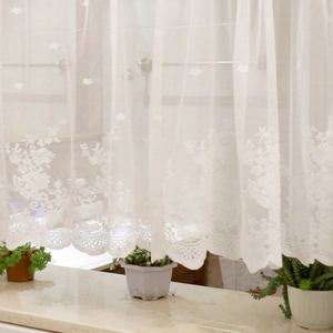 White floral lace sheer curtain with scalloped edge hanging over windowsill plants