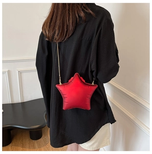 Detail of a red star-shaped crossbody bag with a sleek gold chain on a black shirt
