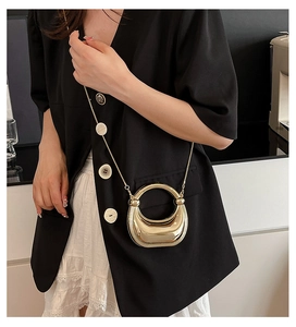 Primer plano de bolso media luna dorado espejo con cadena sobre traje negro