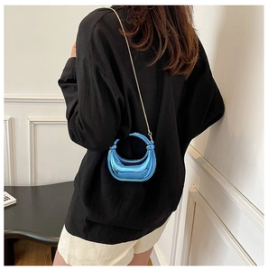 Detalle de mini bolso azul metalizado con cadena dorada sobre el hombro de modelo