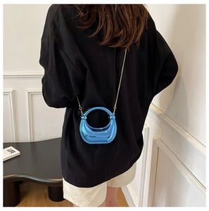Detalle de bolso espejo azul con asa redonda y cadena dorada en entorno moderno
