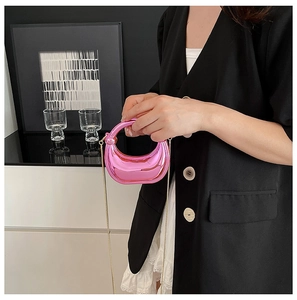 Detalle de un mini bolso de media luna rosa metálico brillante con cadena y asa dorada