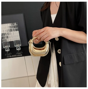 Detalle de bolso de media luna en metal dorado con asa de cadena acrílica y diseño minimalista