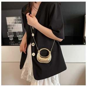 Detalle de un mini bolso de media luna en metal dorado con cadena fina sobre una modelo