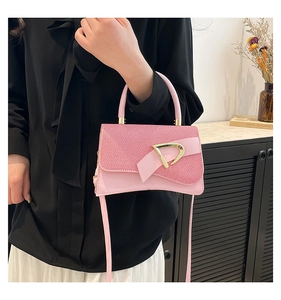 Detail of pink saddle bag featuring textured fabric flap and gold D-shaped metal clasp