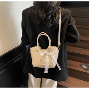 Détail du sac seau crème avec nœud en dentelle et perle sur cuir grainé élégant