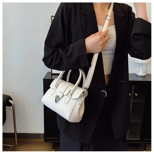 Détail du sac Boston en cuir blanc avec boucle argentée porté avec un costume noir