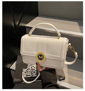 Detail of white quilted leather bag with golden M buckle on a stylish step background