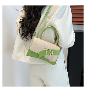 Detail of straw and green leather handbag with gold D buckle shown with white suit