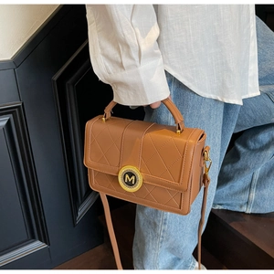 Detail of brown quilted leather handbag featuring a gold M logo and elegant top handle