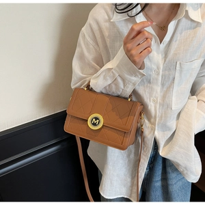 Brown quilted leather handbag worn as a crossbody by a model in a white shirt and jeans