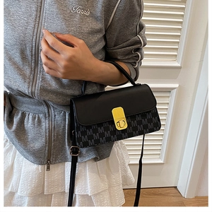 Detail of black crossbody bag with M-letter jacquard pattern and golden lock buckle