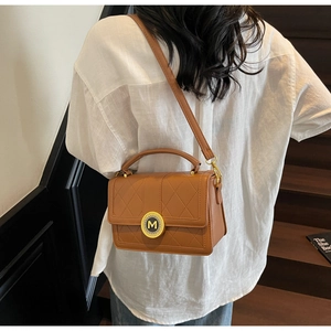 Detail of a brown quilted leather crossbody bag featuring a golden M logo and handle