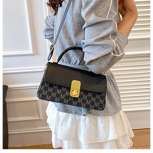 Close-up of matte black leather handbag featuring golden lock and M-patterned canvas