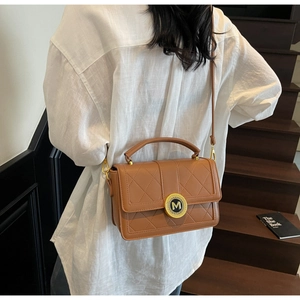 Detail of a brown quilted leather handbag featuring a golden M logo and top handle strap
