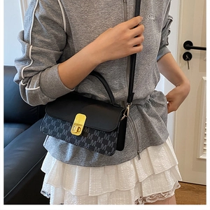 Detail of grey M-letter print and gold turn-lock on a black crossbody messenger bag