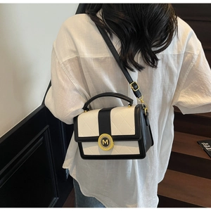 Detail of contrast stitch quilted handbag featuring gold M buckle and leather strap