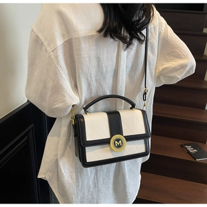 Detail of a chic quilted black and white crossbody bag with a gold M-logo metal buckle
