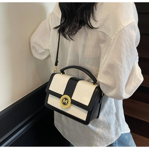 Detail of retro monochrome quilted handbag with gold M-logo buckle worn over the shoulder