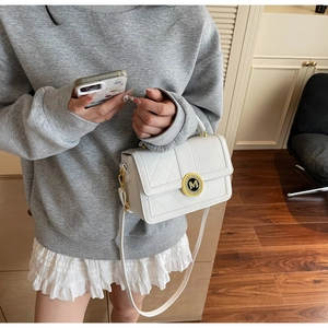 Close-up of a white quilted crossbody bag with a gold M-letter logo buckle and strap