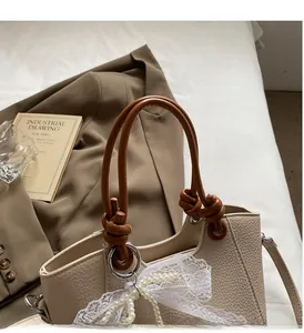 Détail du sac à main beige grainé avec nœud en dentelle et pendentif de perles élégant