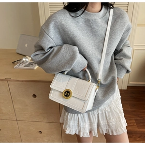 Detail of white quilted leather handbag with gold M logo buckle and adjustable shoulder strap