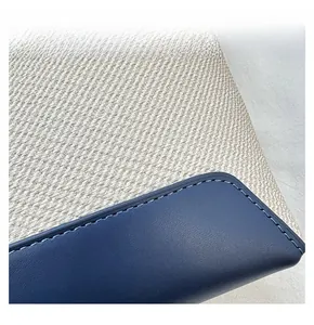 Detail display of tight blue stitching on beige woven fabric and leather shoulder bag