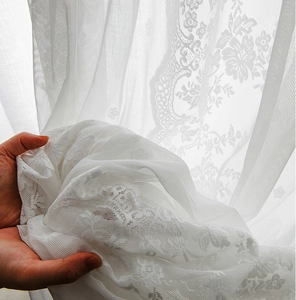 Detailed view of white floral lace curtain fabric with sheer mesh texture and patterns