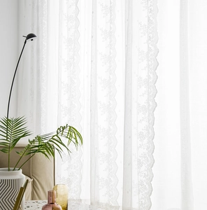 Close-up of white lace curtain featuring floral embroidery and elegant wavy edges