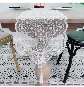 Detailed view of white lace table runner with hollow embroidery and elegant long tassels