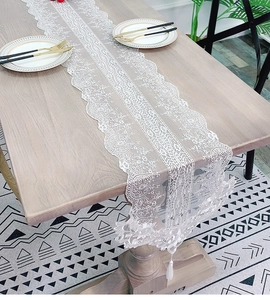 Close-up of white lace table runner with intricate embroidery and elegant fringe tassels