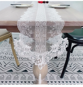 Detail view of white floral lace table runner with elegant fringe on wood furniture