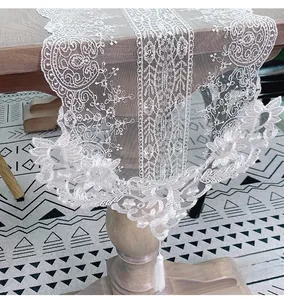Detailed view of white floral lace table runner with elegant tassels and scalloped edges