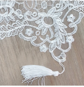 Macro shot of white lace table runner with floral embroidery and tassel details