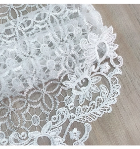 Close-up of white lace fabric with floral embroidery on a natural wooden background