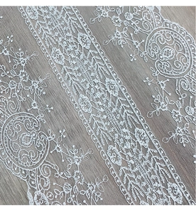 Detailed view of white floral lace fabric with intricate mesh embroidery and wavy edges