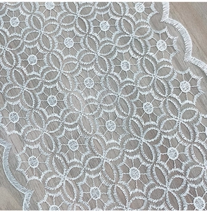 Detail of white lace table runner featuring floral embroidery and scalloped edges