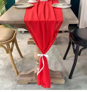 Detail of red chiffon table runner with white ribbon ties on a wooden dining table