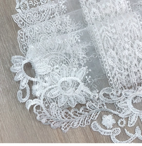 Macro shot of white floral lace runner featuring detailed embroidery on a grey wood surface