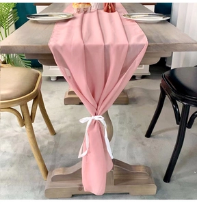 Pink chiffon table runner with white silk ribbon tie on dark wood dining table decoration