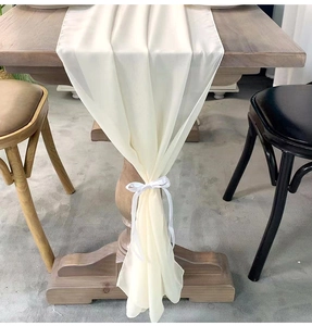 Detail of cream chiffon table runner with decorative ribbon tie on dark wooden table