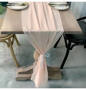 Detail of light pink chiffon table runner with elegant white ribbon tie on wooden table