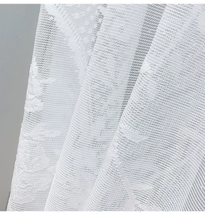 Macro shot of white lace curtain fabric showing detailed floral texture and mesh patterns