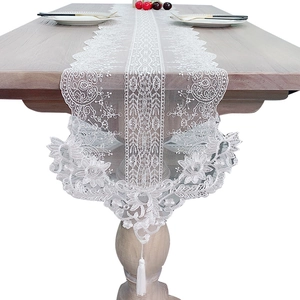 Elegant white floral lace table runner with tassels on a wooden dining table