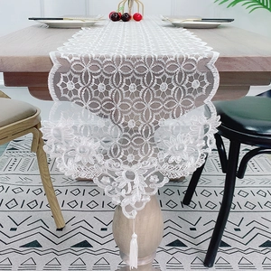 White lace table runner with hollow floral patterns and tassels on a wooden surface